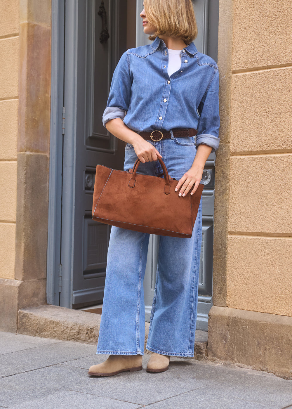 Woman wearing denim shirt and wide-leg jeans, holding a brown suede handbag and wearing camel suede ankle boots — Viscata Cremona boots casual street look.