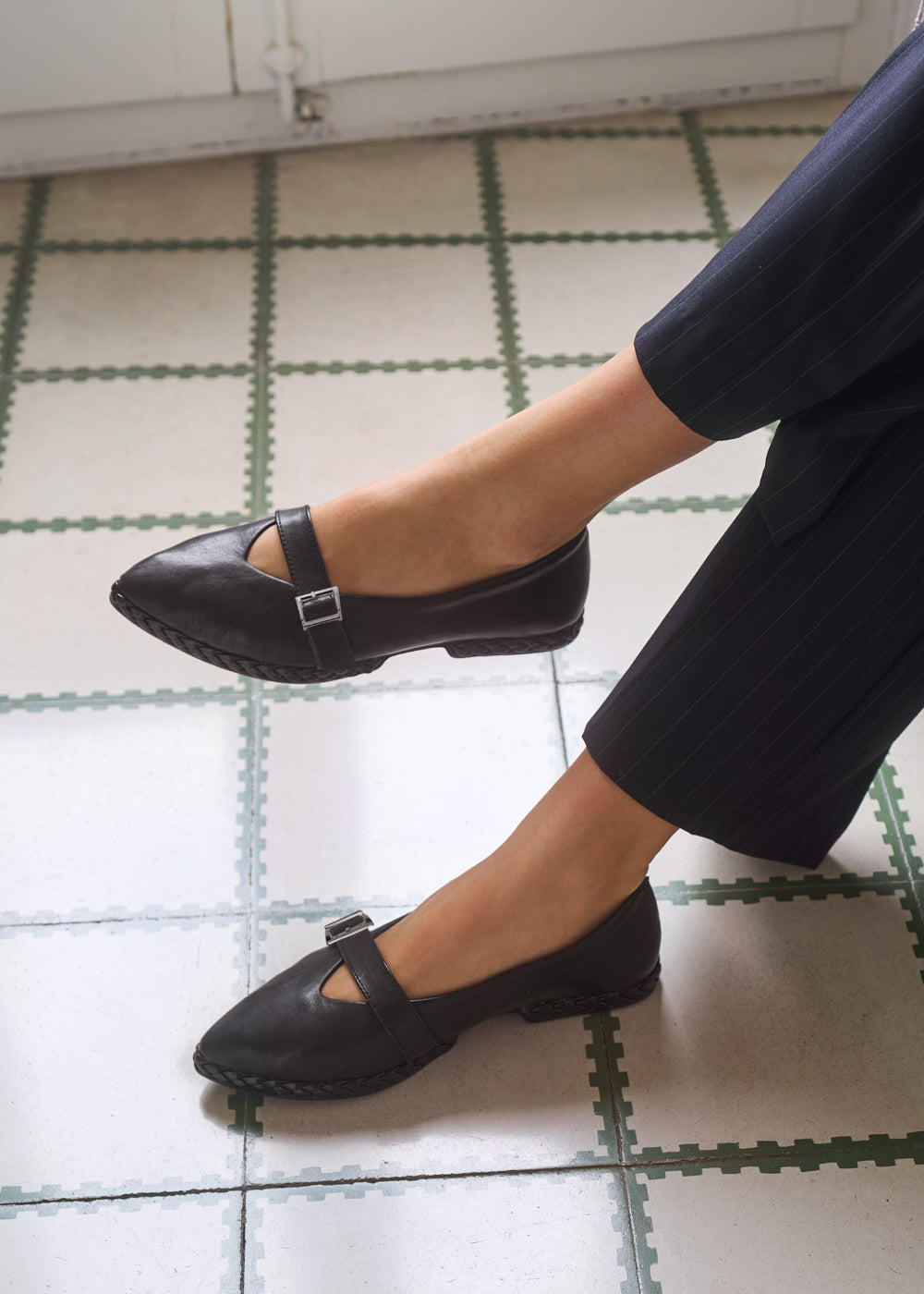 Close-up of woman’s feet wearing black leather Mary Jane flats with silver buckle strap, styled with dark pinstripe pants — Viscata Remini black flats detail shot.