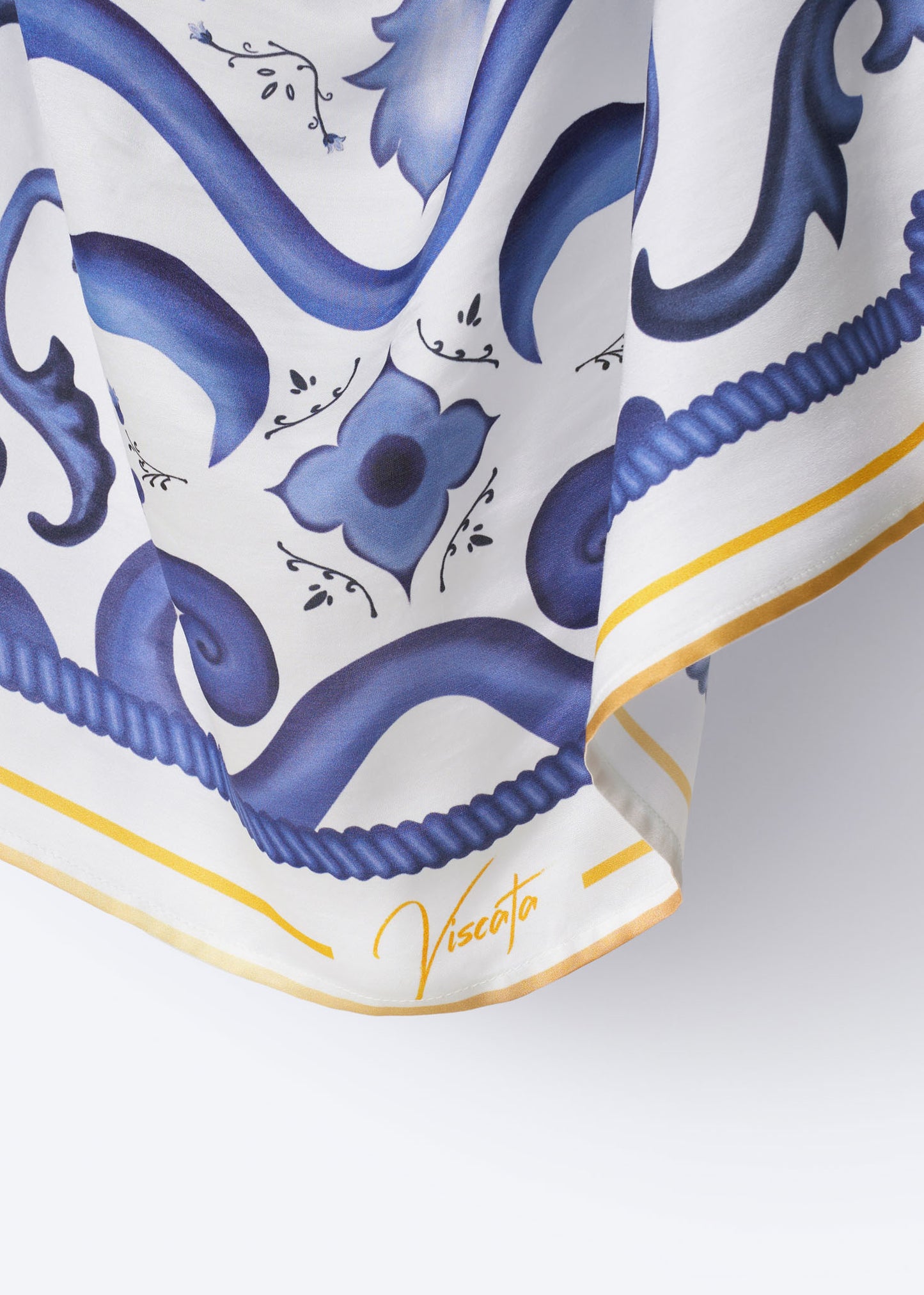 Detail view of Viscata silk scarf corner showcasing signature branding, golden yellow trim, and ornate cobalt blue floral tile pattern – refined Mediterranean accessory with artisan finish