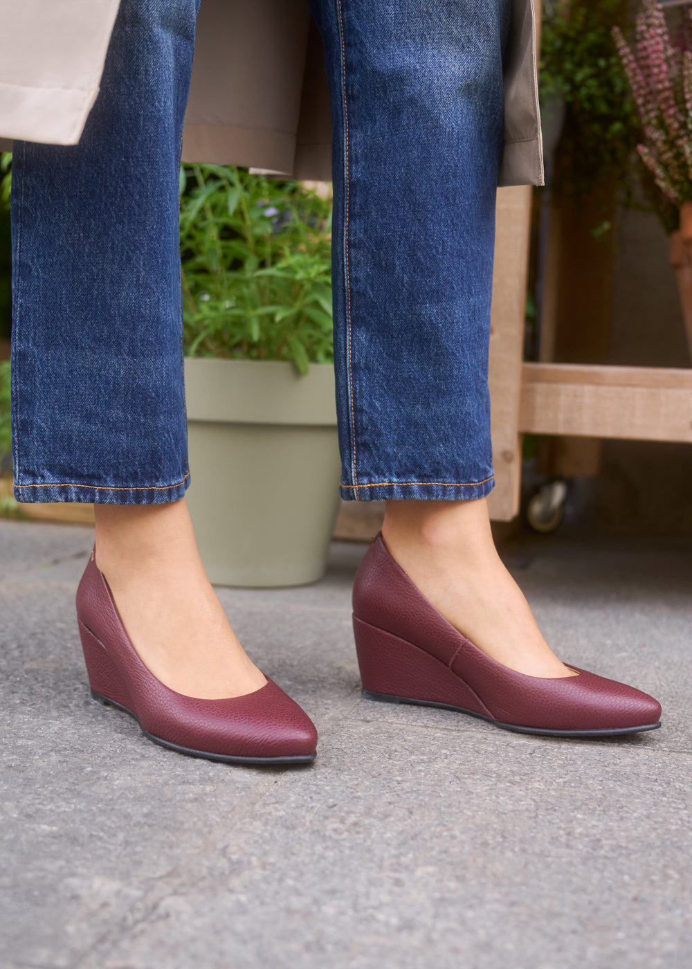 Woman wearing grain burgundy leather wedge shoes paired with cropped blue jeans and a trench coat — Viscata Essenza collection, where everyday elegance meets all-day comfort.