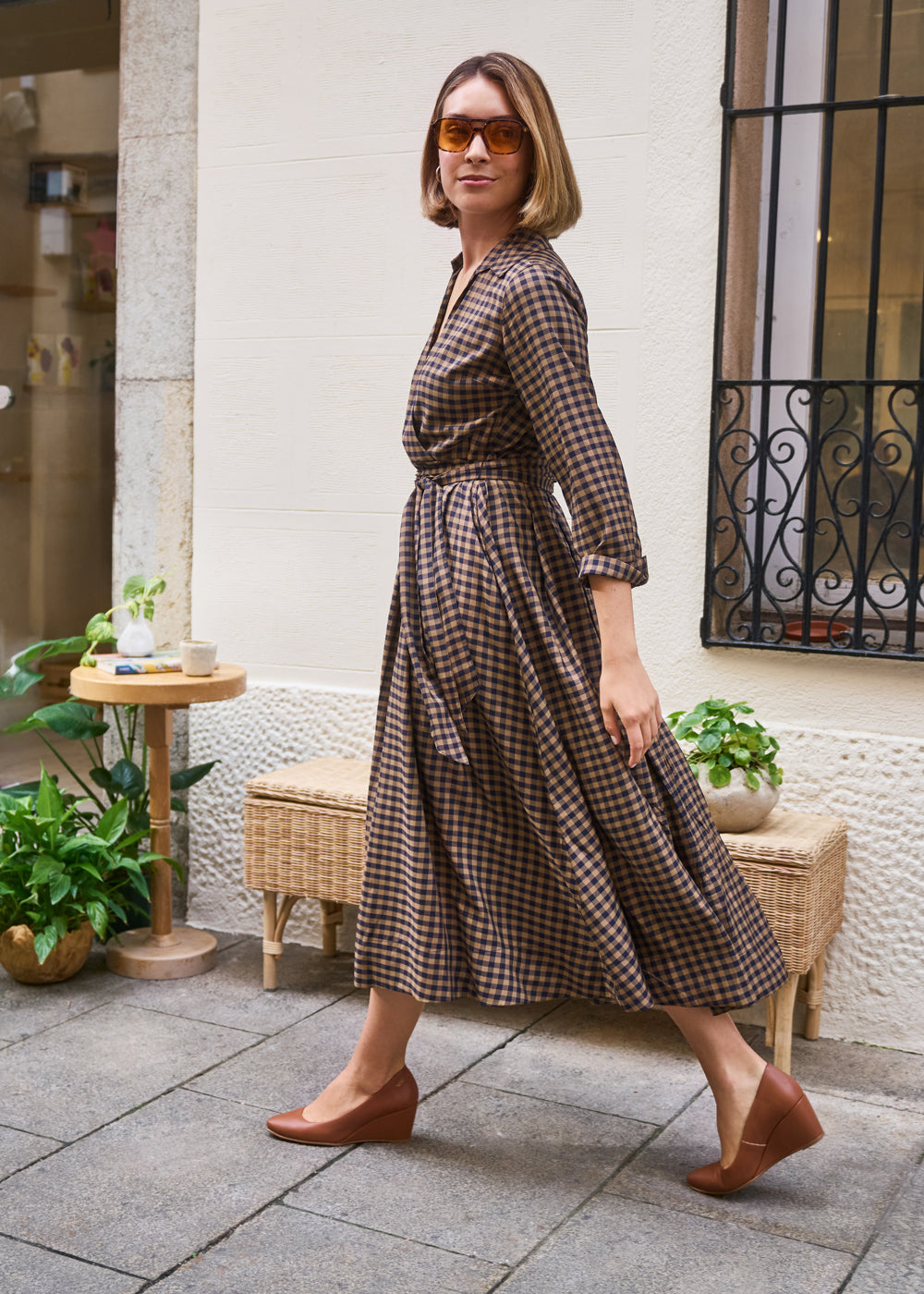 Woman walking outdoors in a brown checkered midi dress styled with tan leather wedge shoes — Viscata Essenza collection, effortless autumn chic.
