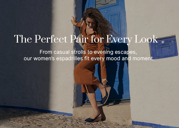 Woman wearing burnt orange outfit and navy slingback espadrille medium wedges, leaning playfully against a blue door on a cobblestone street