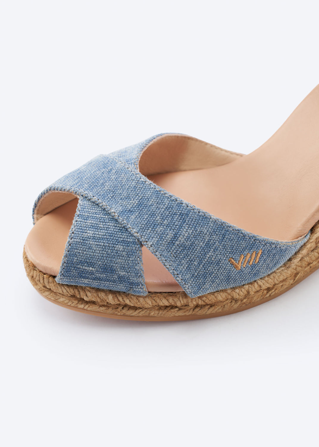 Close-up of washed denim wedge espadrille sandal with crossover front straps and a natural braided jute sole, handcrafted in Spain