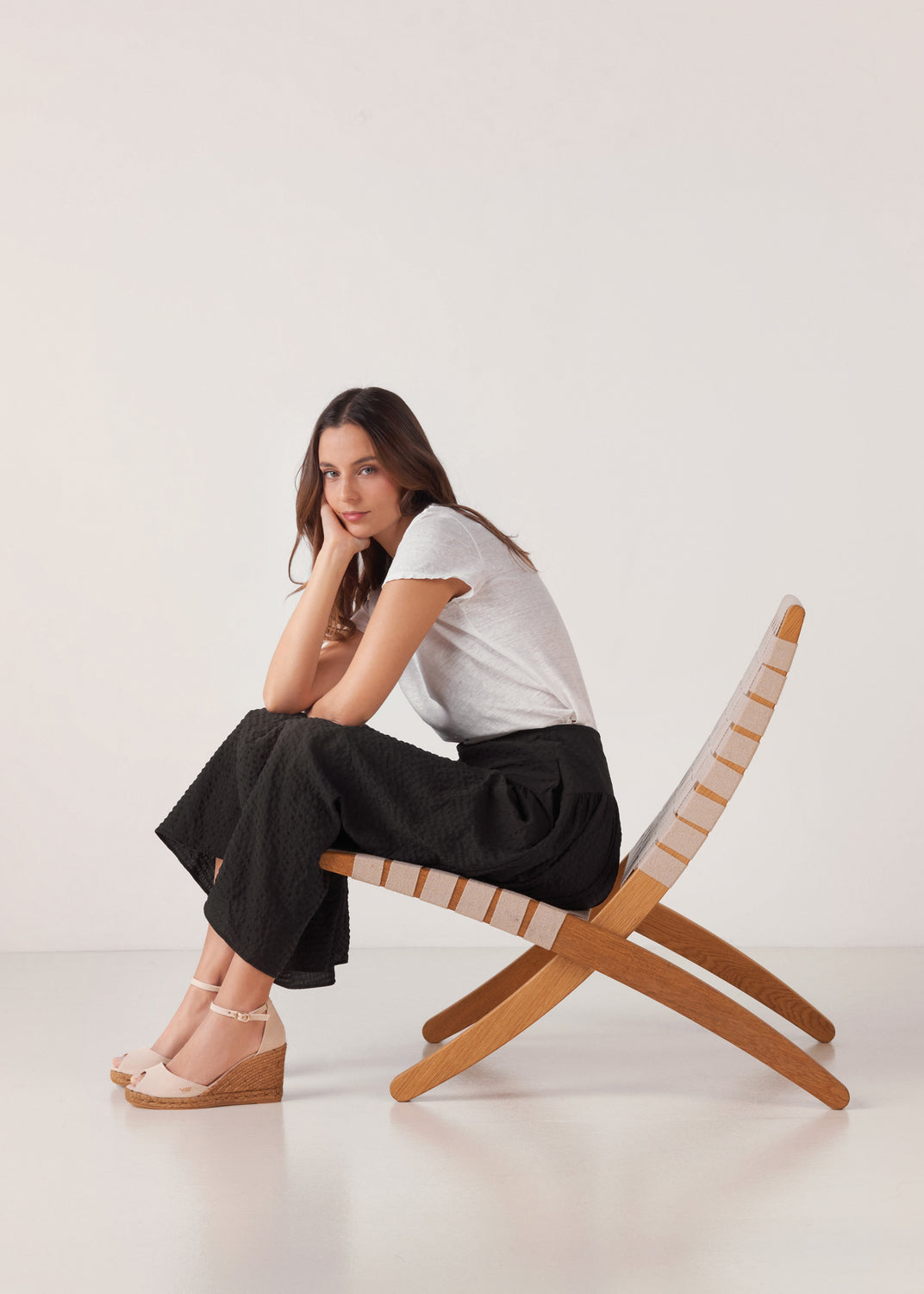 Seated model wearing beige canvas ankle-strap wedge espadrilles with a natural jute platform