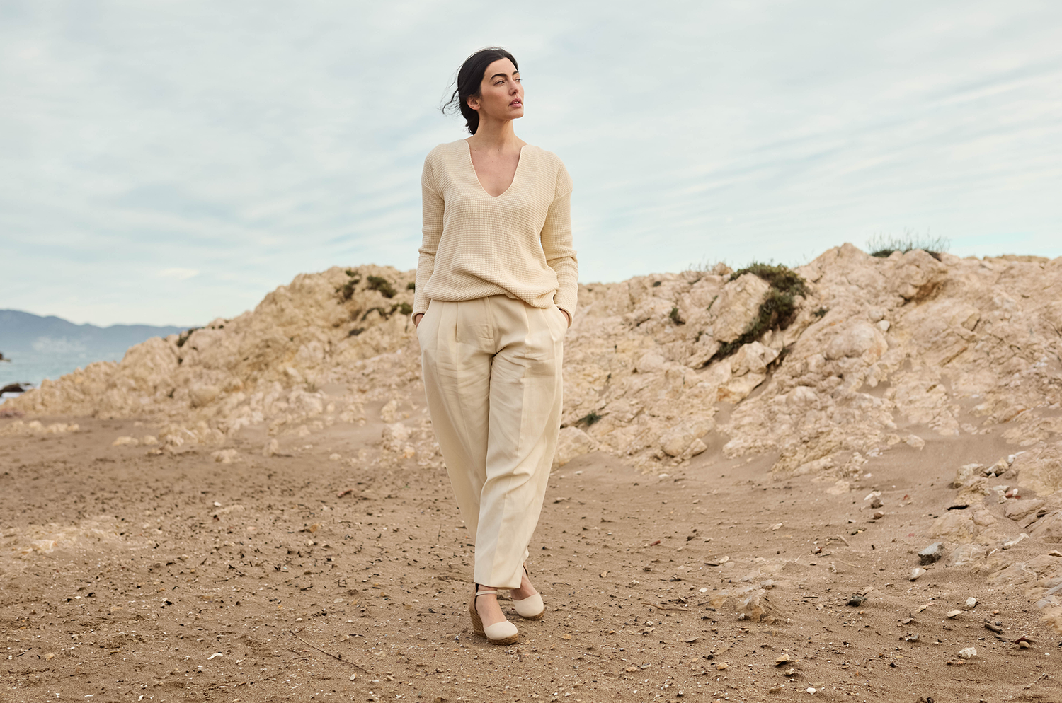 Woman in beige outfit standing on a rocky beach