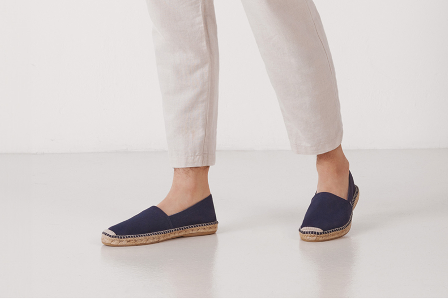 Person wearing navy espadrilles and white pants on a light background