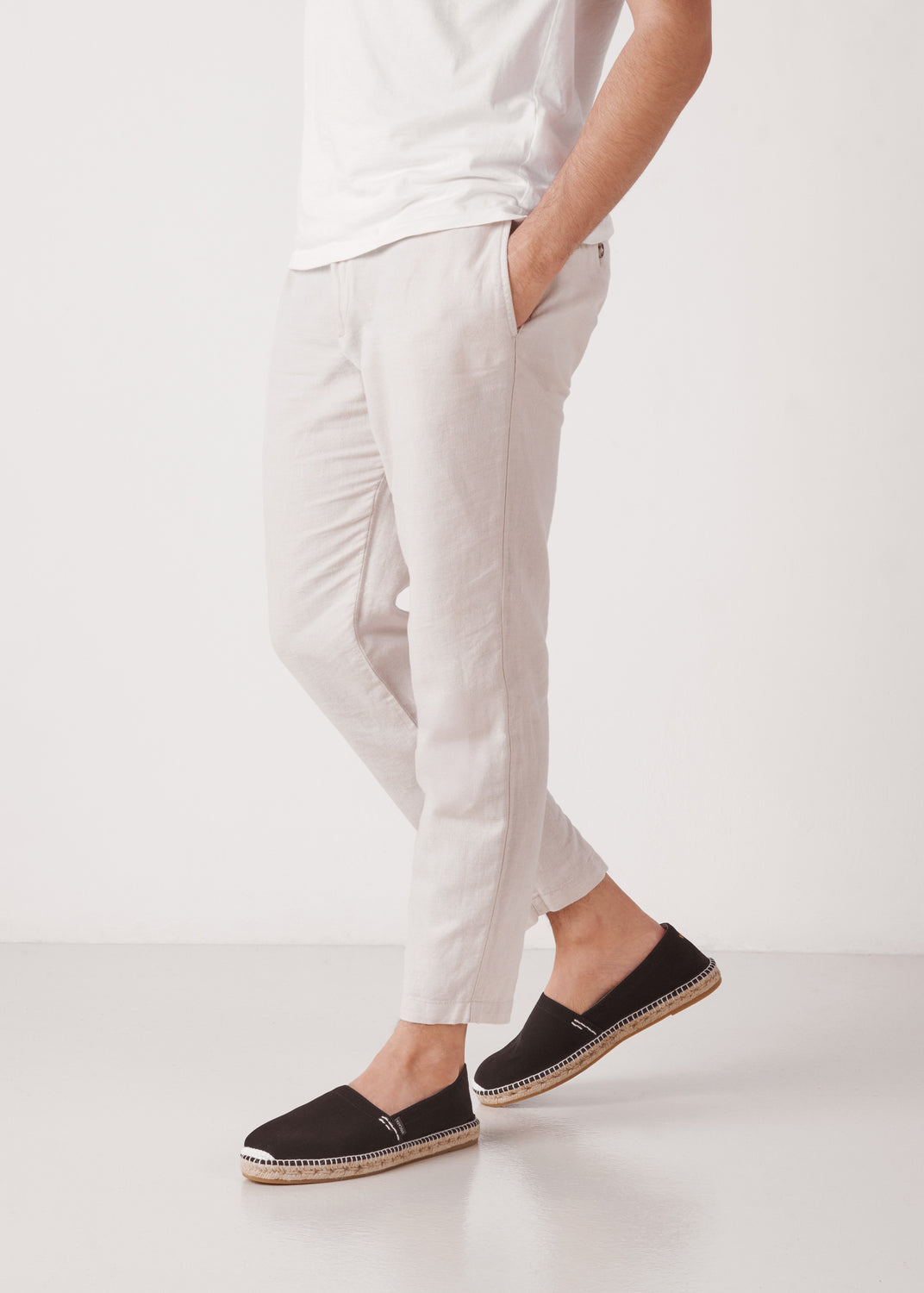 Male model walking in black canvas slip-on men’s espadrilles with braided jute sole, studio background.