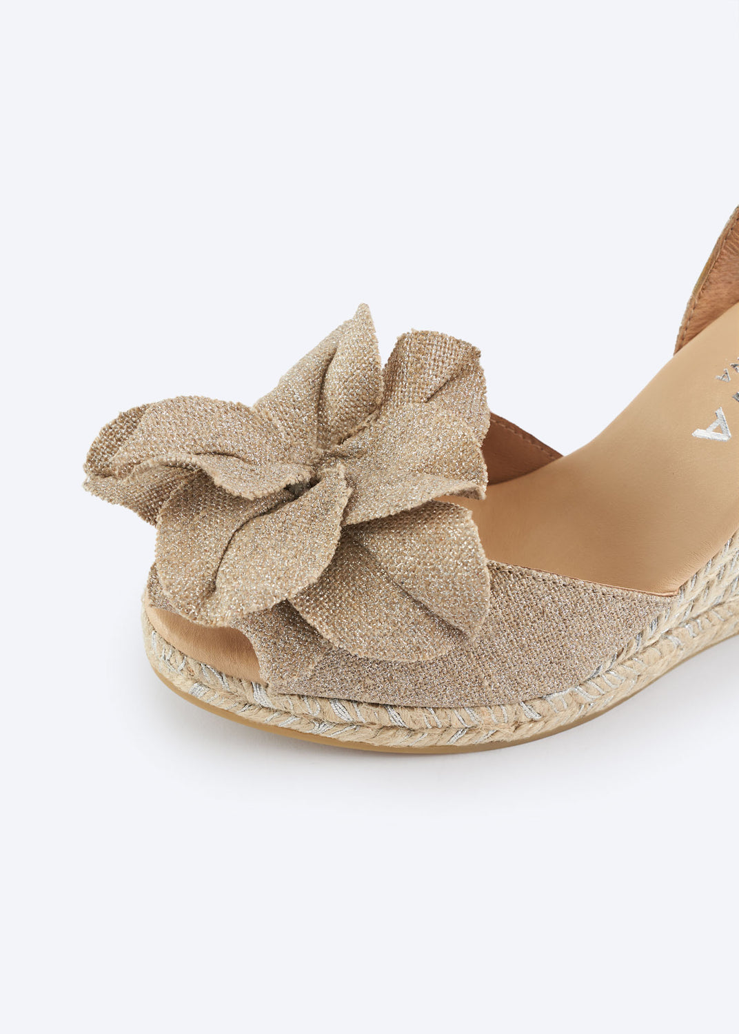 Close-up of silver metallic espadrille wedge sandal with oversized bow detail and braided jute sole woven with silver threads.