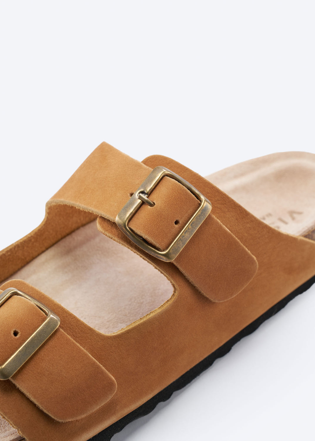 Close-up of a camel suede slide sandal with double buckles.