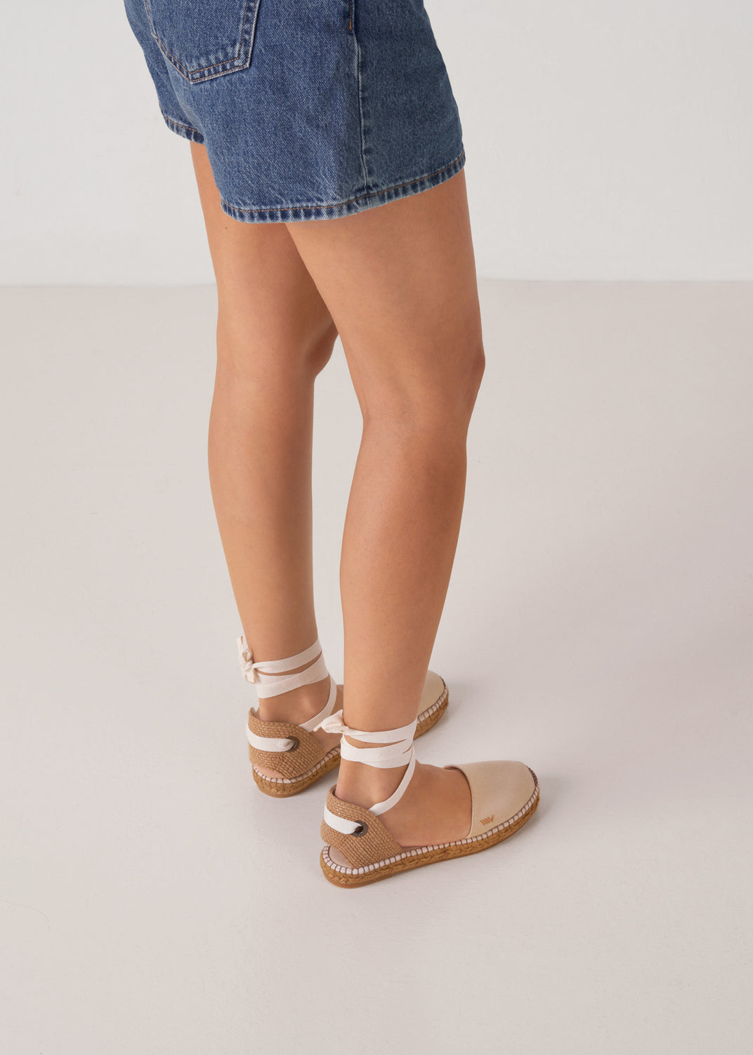 Back view of beige canvas lace-up flat espadrilles with ankle ties and a natural jute sole on model