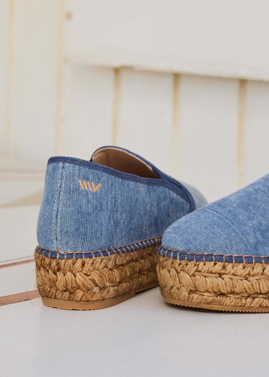 Close-up of blue denim espadrille slip-ons highlighting the jute sole and stitching detail.