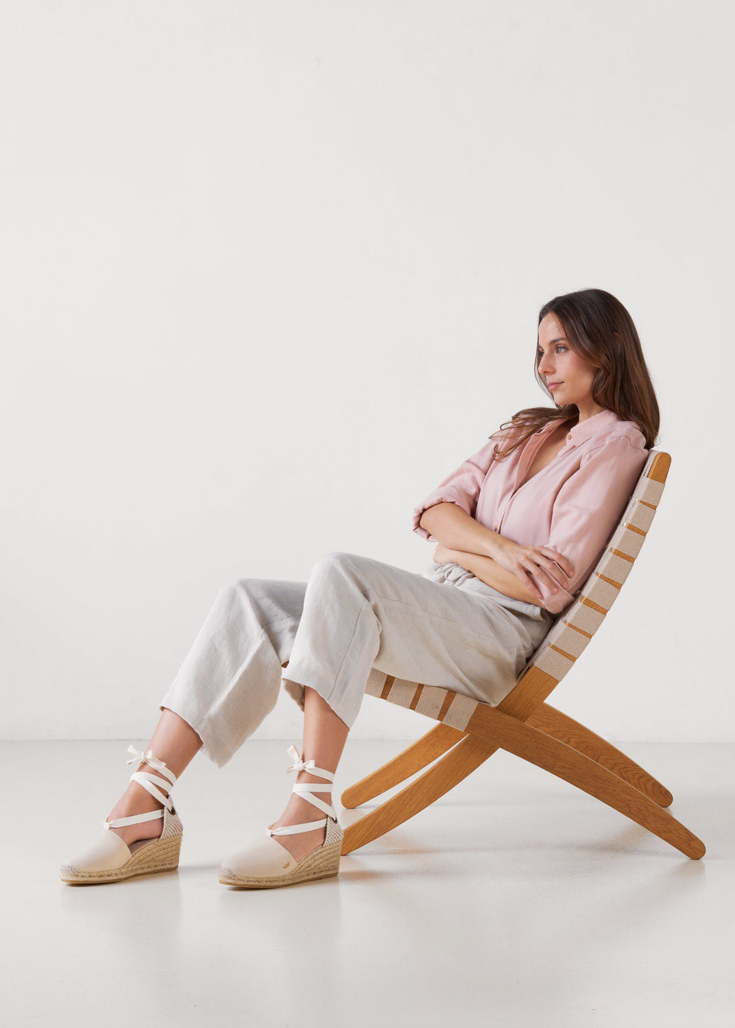 Model seated wearing beige canvas lace-up wedge espadrilles with ankle ties and a natural jute platform
