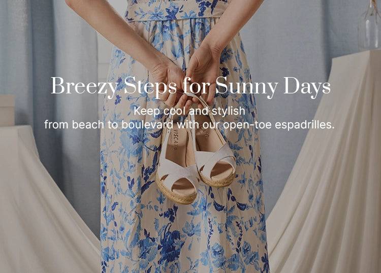 Woman in a blue-and-white floral dress holding a pair of white open crossed-toe espadrille wedges with ankle straps from Viscata, showcasing breathable summer footwear handcrafted in Spain