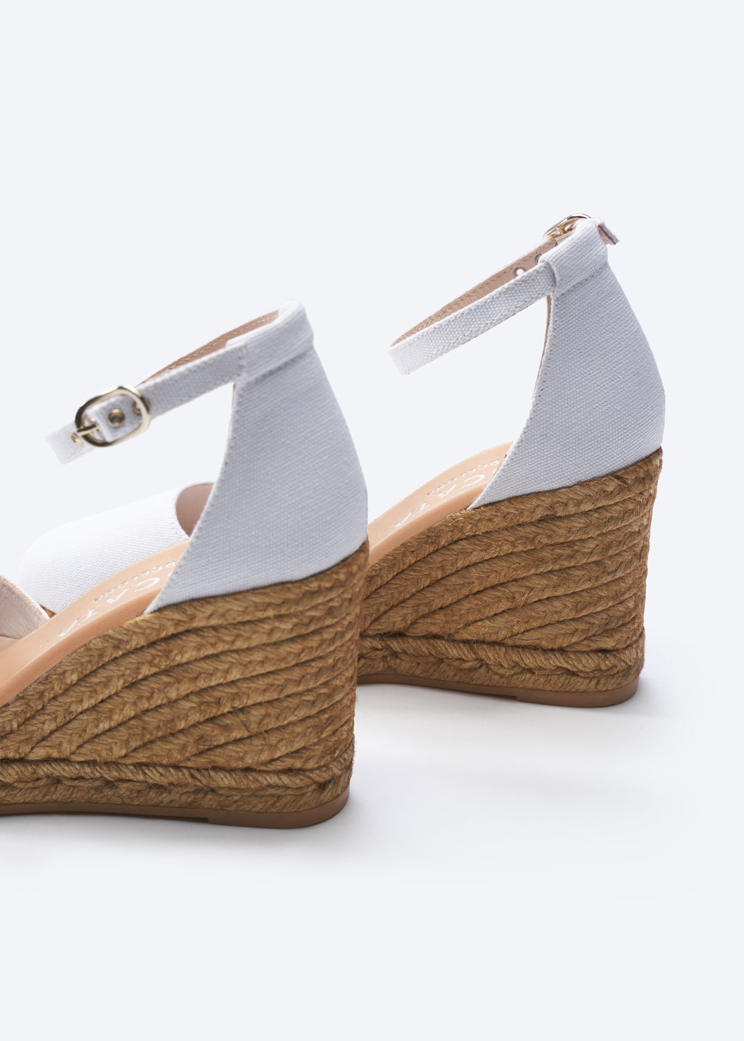 Wedge sandals with white straps and brown woven sole on a white background