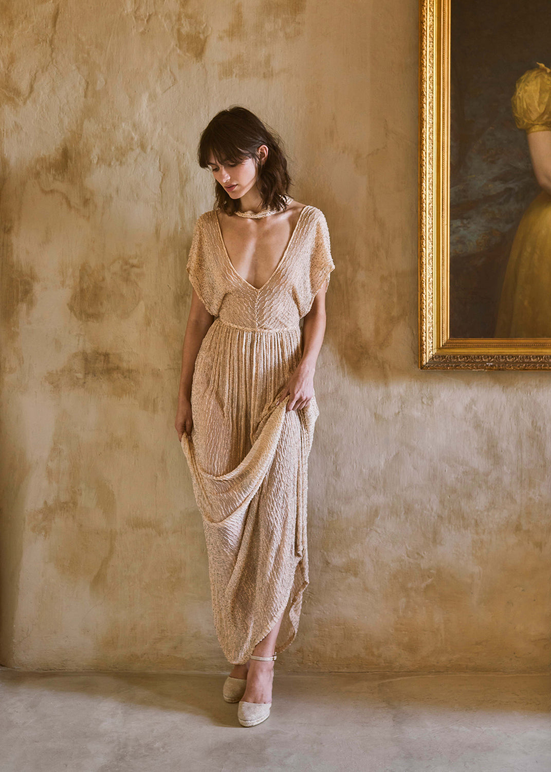 Woman wearing champagne gold espadrille wedges styled with a flowing textured dress in an elegant Mediterranean interior.