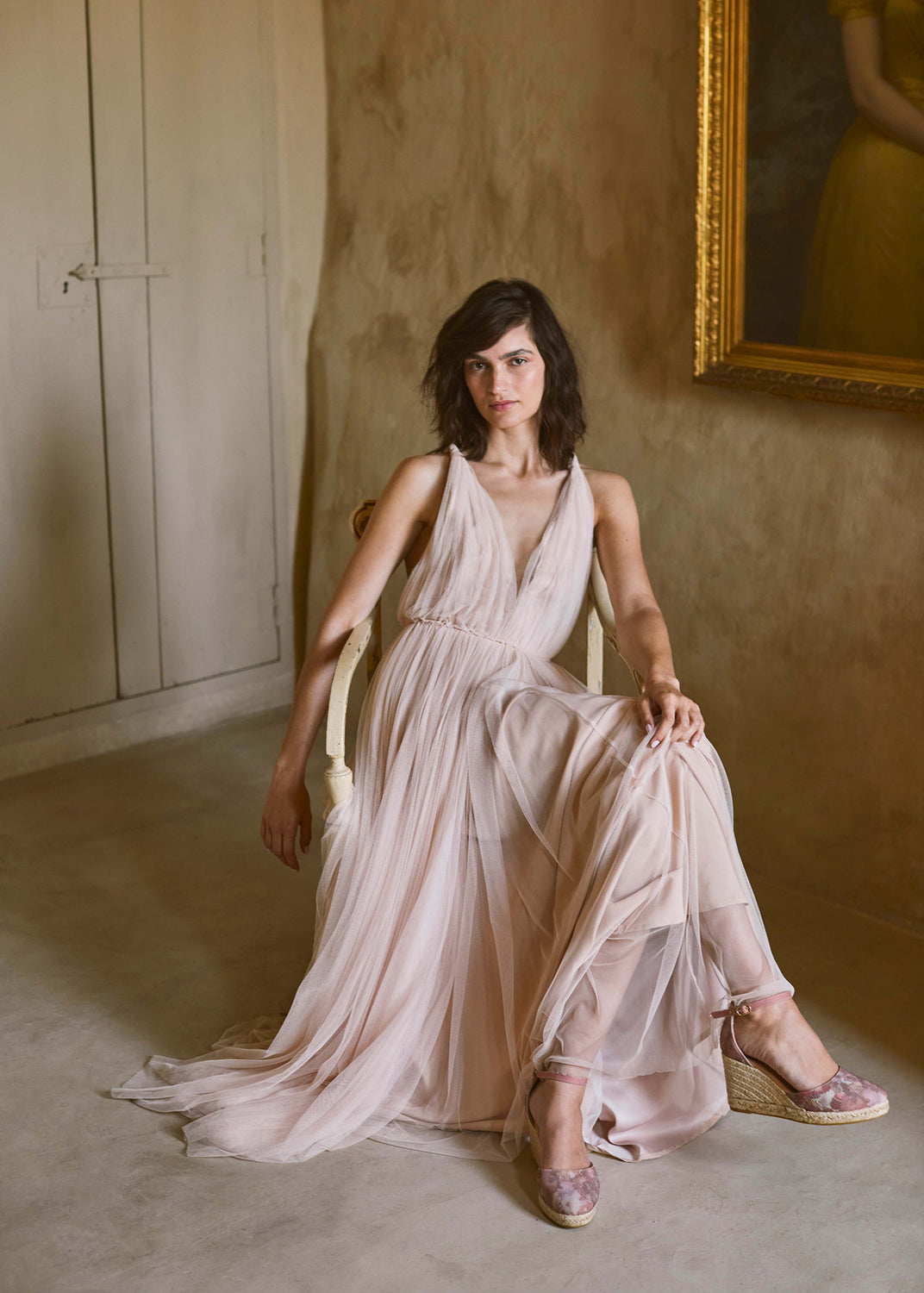 Woman wearing pink floral espadrille wedges with ankle straps, styled with a flowing blush dress in an elegant Mediterranean interior.