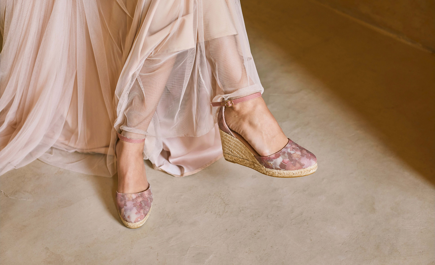 Pink floral espadrille wedges styled beneath a flowing blush tulle dress in a softly lit Mediterranean interior.
