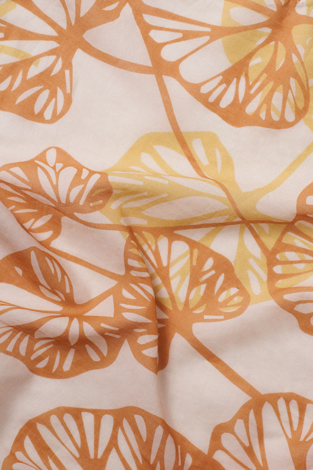 Close-up of the Orange Petals foulard, featuring layered leaf silhouettes in warm orange and yellow on a soft peach fabric with gentle natural folds