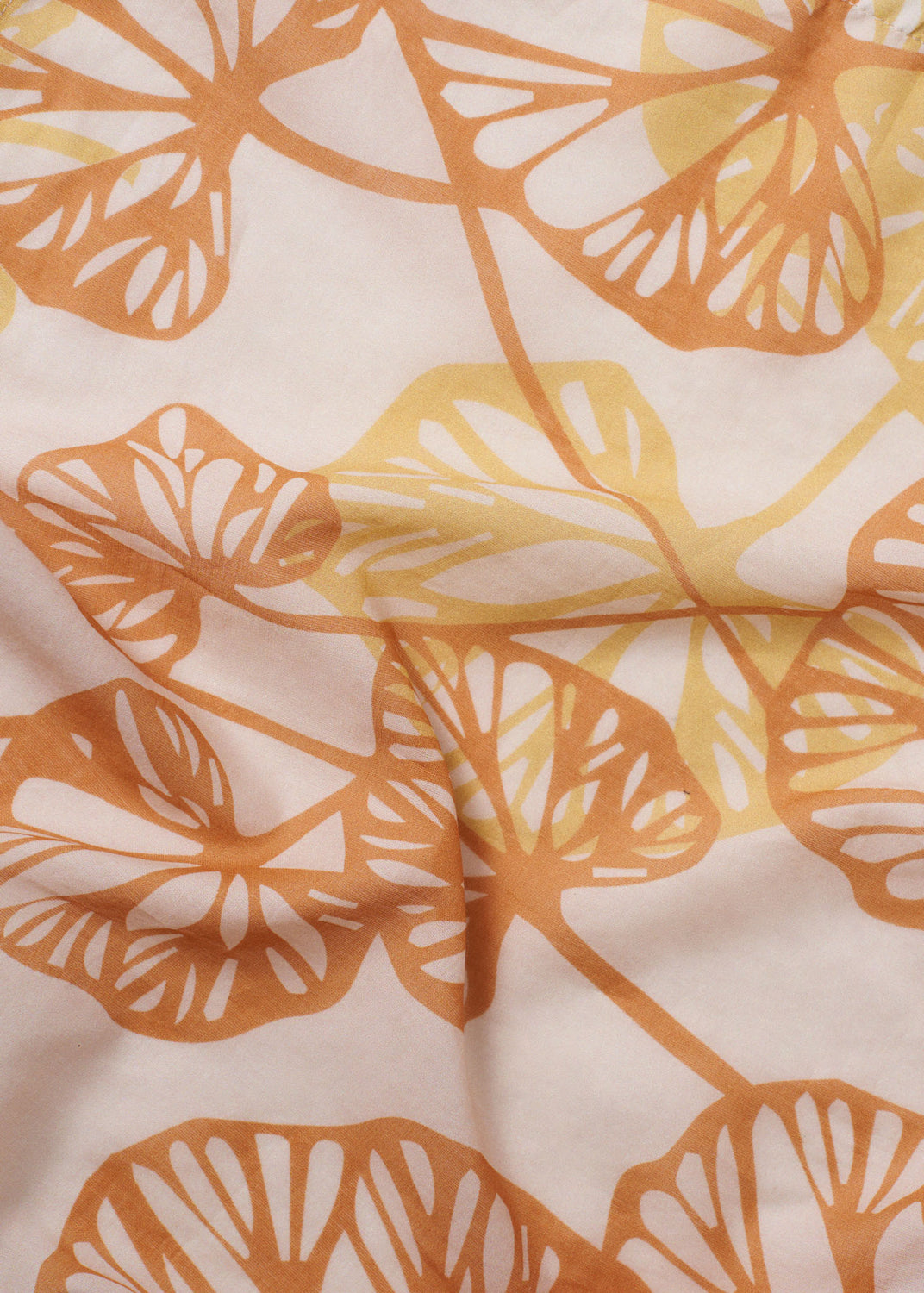 Close-up of the Orange Petals foulard, featuring layered leaf silhouettes in warm orange and yellow on a soft peach fabric with gentle natural folds