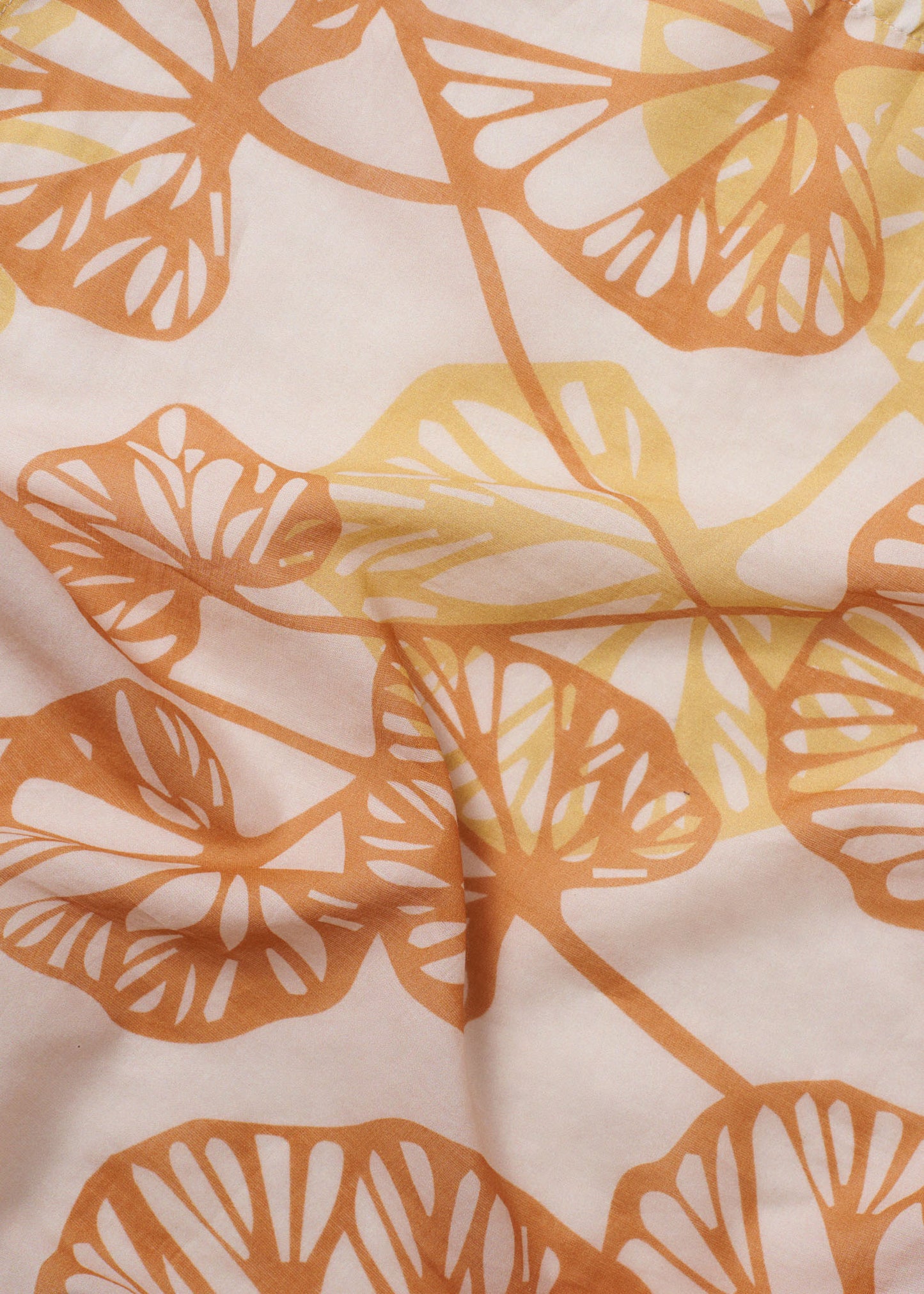 Close-up of the Orange Petals foulard, featuring layered leaf silhouettes in warm orange and yellow on a soft peach fabric with gentle natural folds
