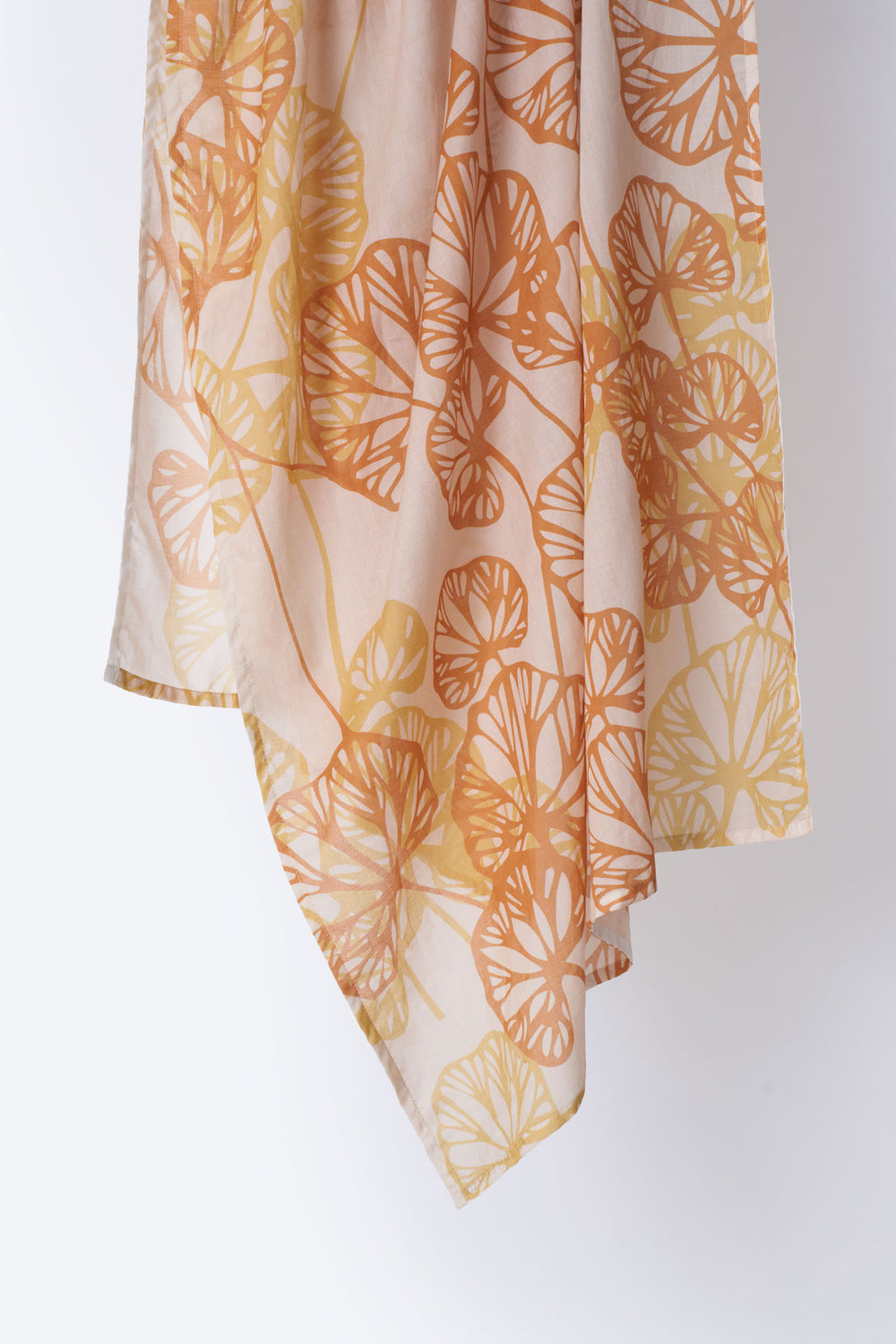 Close-up of soft cotton scarf in blush pink with overlapping orange and yellow leaf silhouettes – lightweight, breathable fabric with a delicate drape, ideal for spring and summer wear