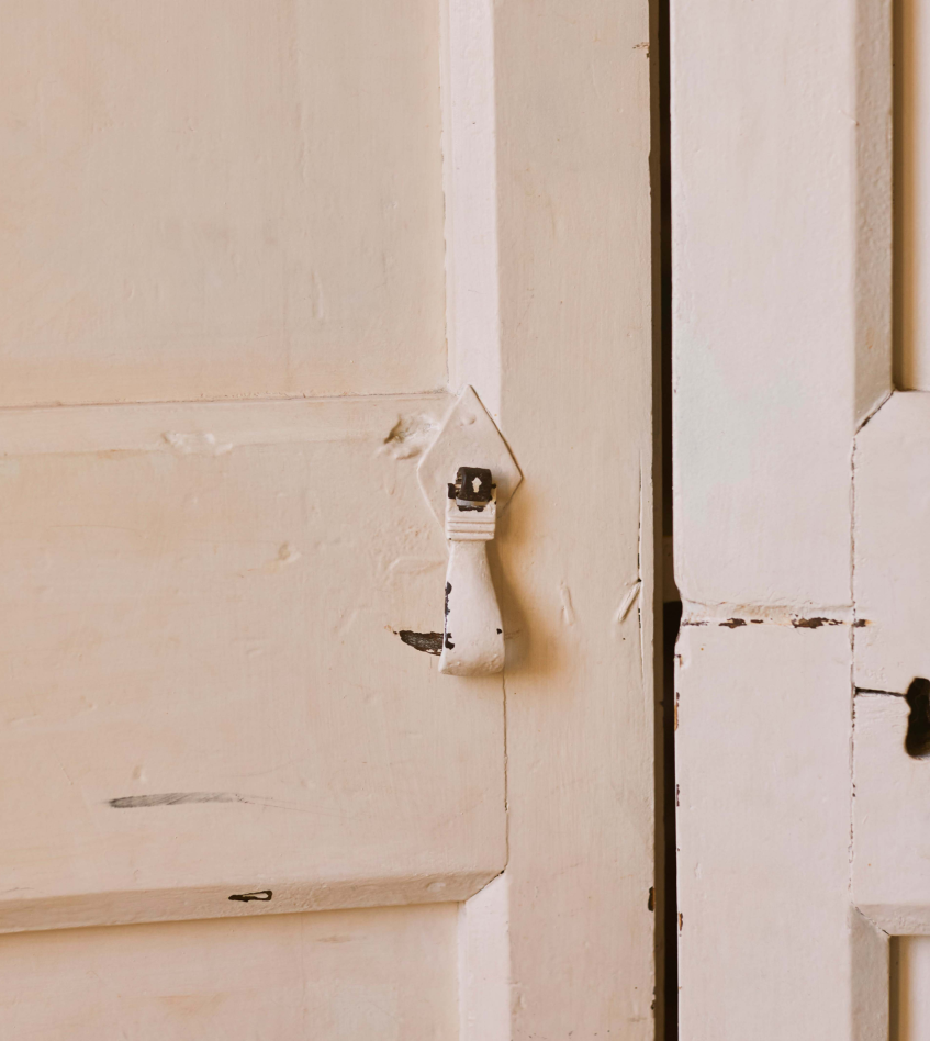 Minimalist Mediterranean interior detail featuring a rustic painted door and vintage handle in warm natural light.