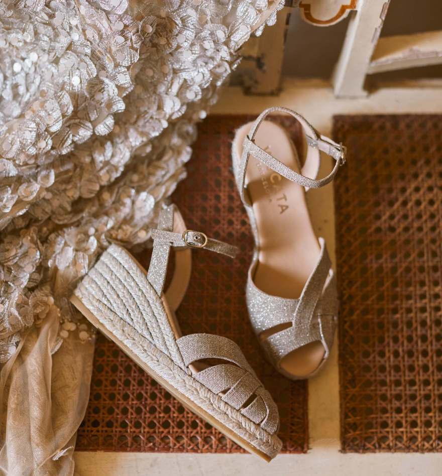 Metallic champagne espadrille wedge sandals styled beside an embellished evening dress in a warm Mediterranean interior.
