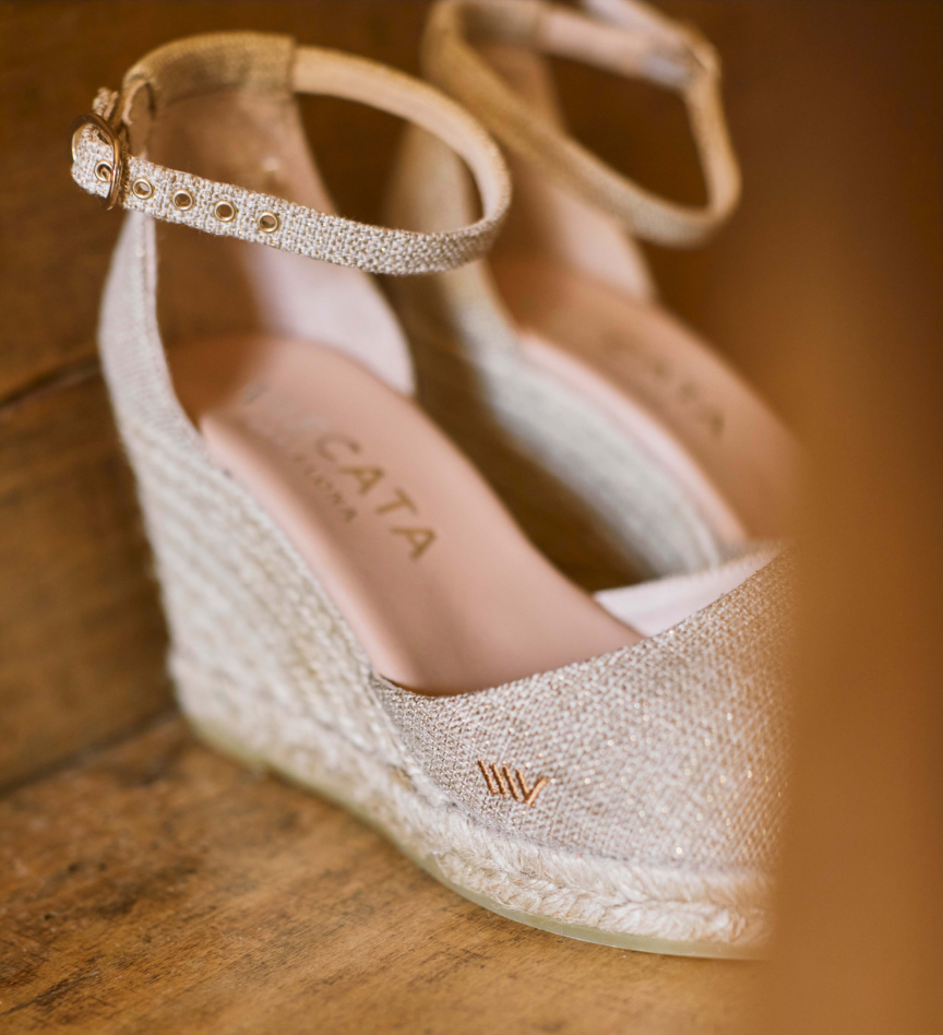 Metallic champagne espadrille wedge shoes photographed in warm natural light on a rustic wooden surface.