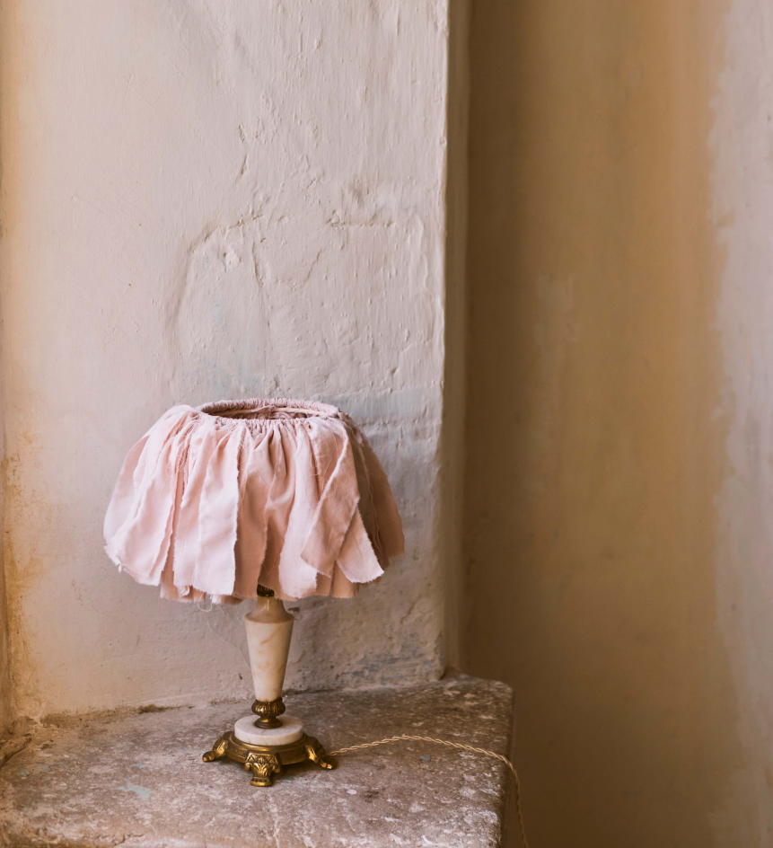 Decorative blush fabric table lamp placed on a stone ledge in a warm Mediterranean interior.