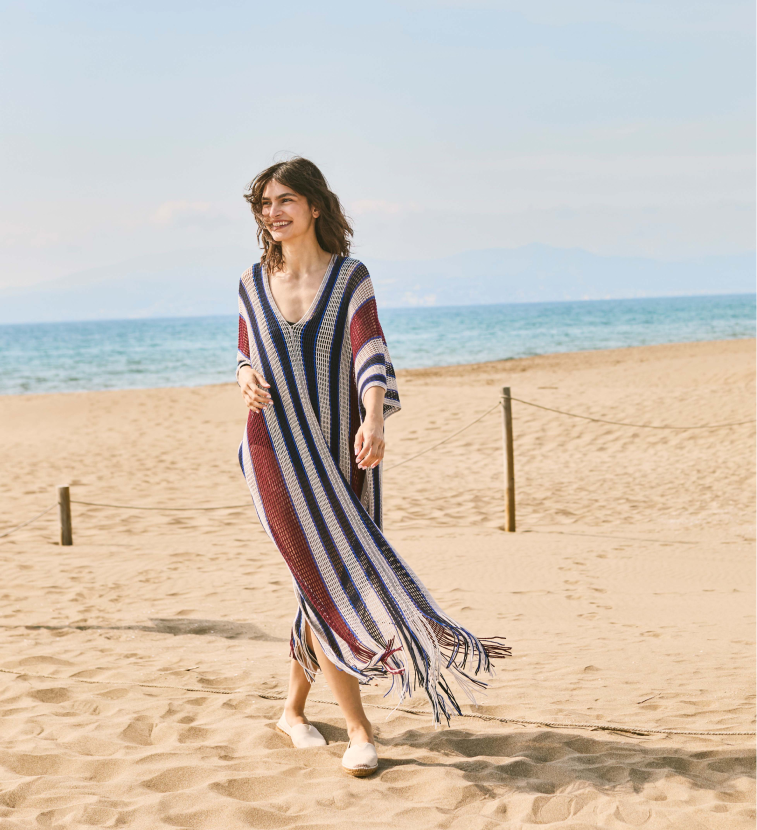 Beige espadrille flats on a sandy beach, styled with a striped fringed cover-up for breezy Mediterranean days