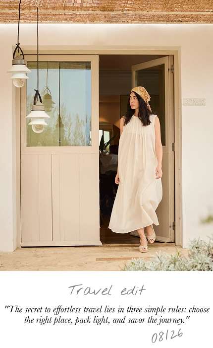 A woman wearing a cream-colored sleeveless maxi dress and a straw hat stands in a doorway of a rustic beige building. The image includes a text overlay at the bottom that reads 'Travel edit' with a quote about travel.