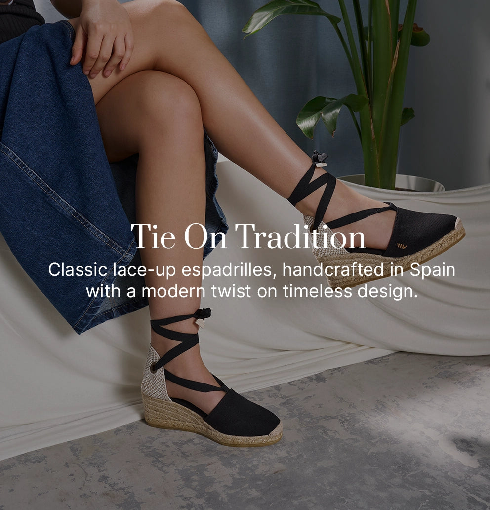 Woman wearing black lace-up wedge espadrilles by Viscata, handcrafted in Spain with traditional jute soles, styled with a denim skirt indoors