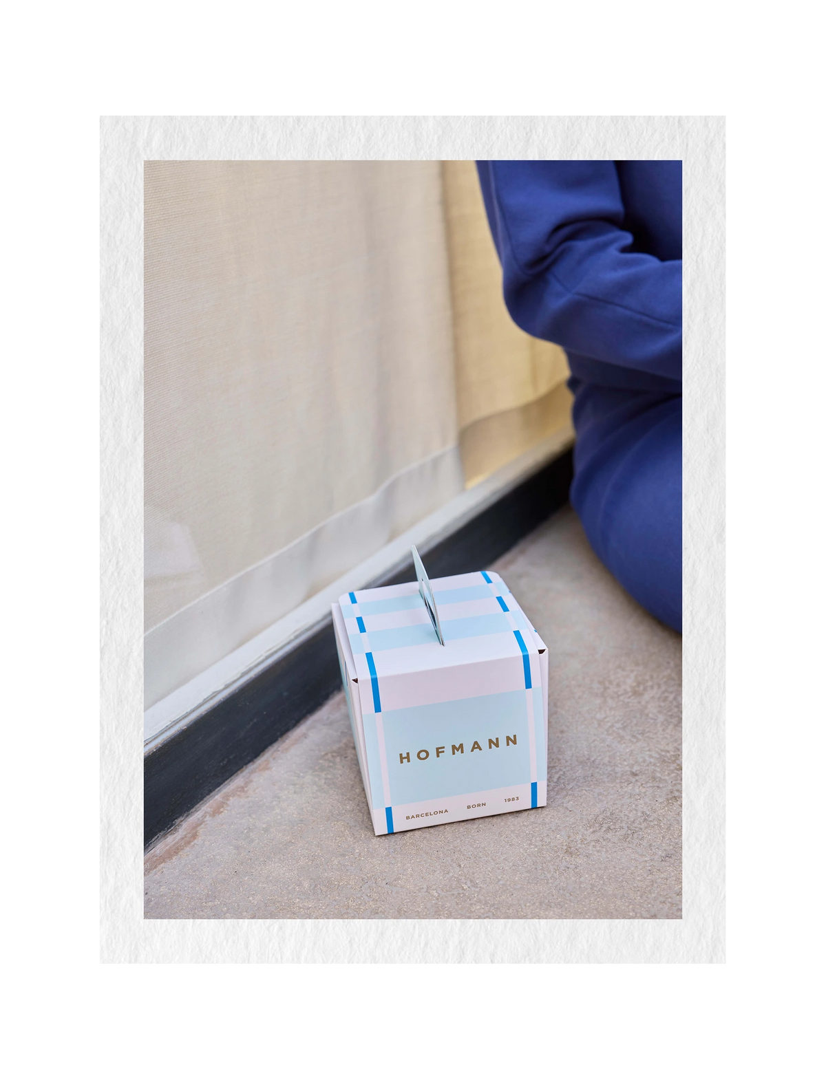 A Hofmann chocolate box sits on a concrete floor next to a window with a person wearing a blue hoodie partially visible in the background.