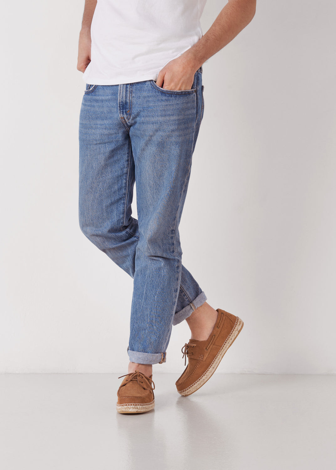 Man wearing cuffed blue jeans styled with tan suede espadrille boat shoes with lace detail and jute-wrapped soles.