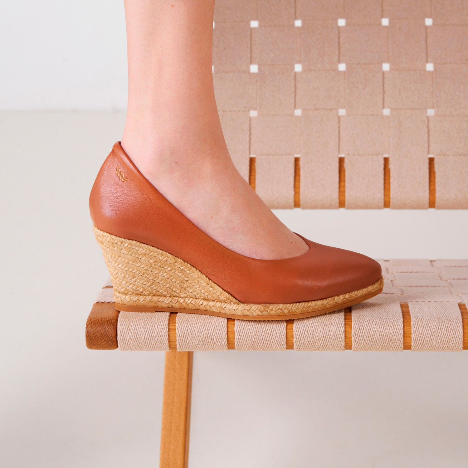 Close-up of a whiskey brown leather espadrille wedge pump with a braided jute sole, side view