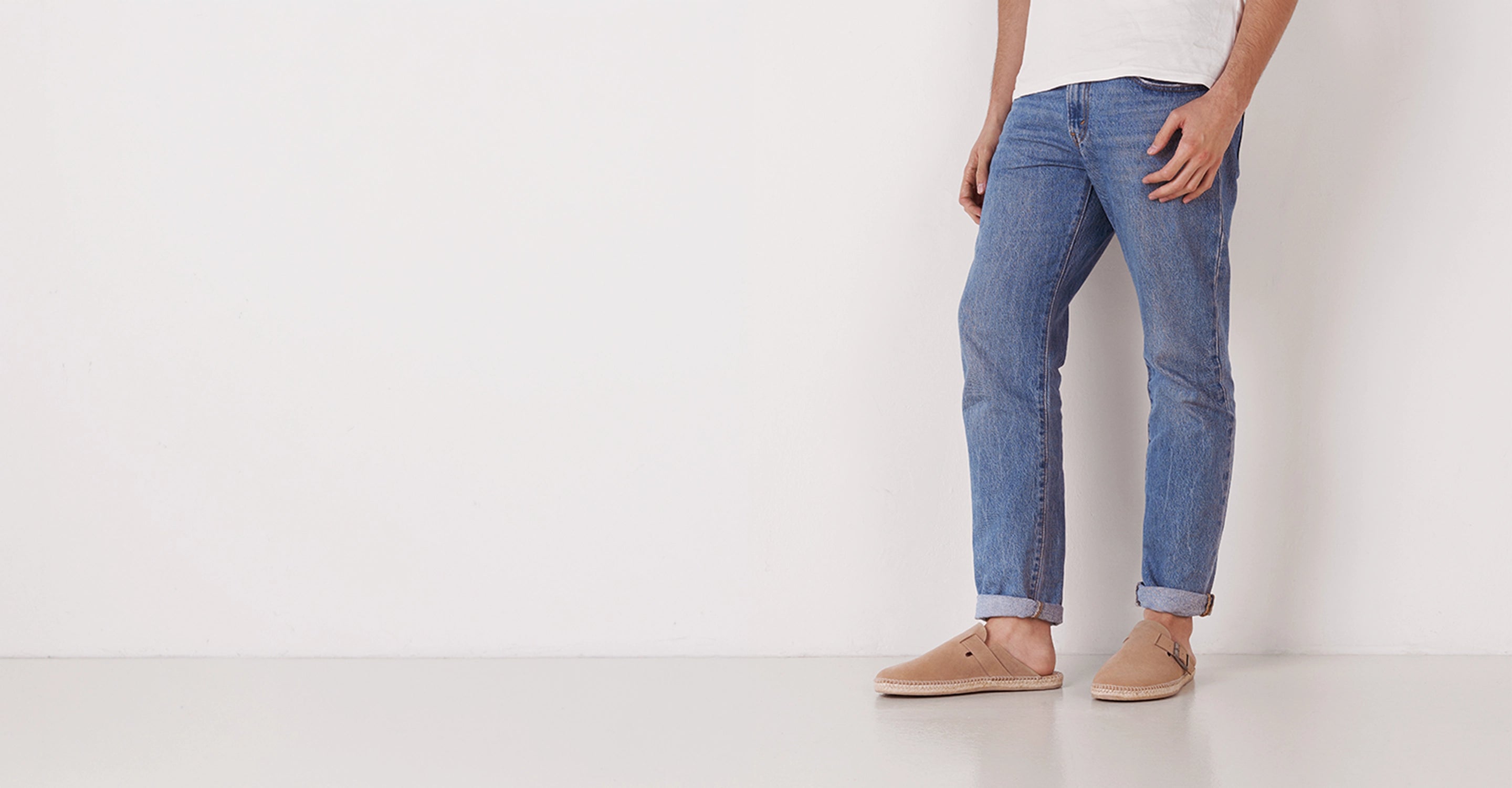 A man wearing blue jeans paired with Raco camel sabot espadrilles standing against a white background