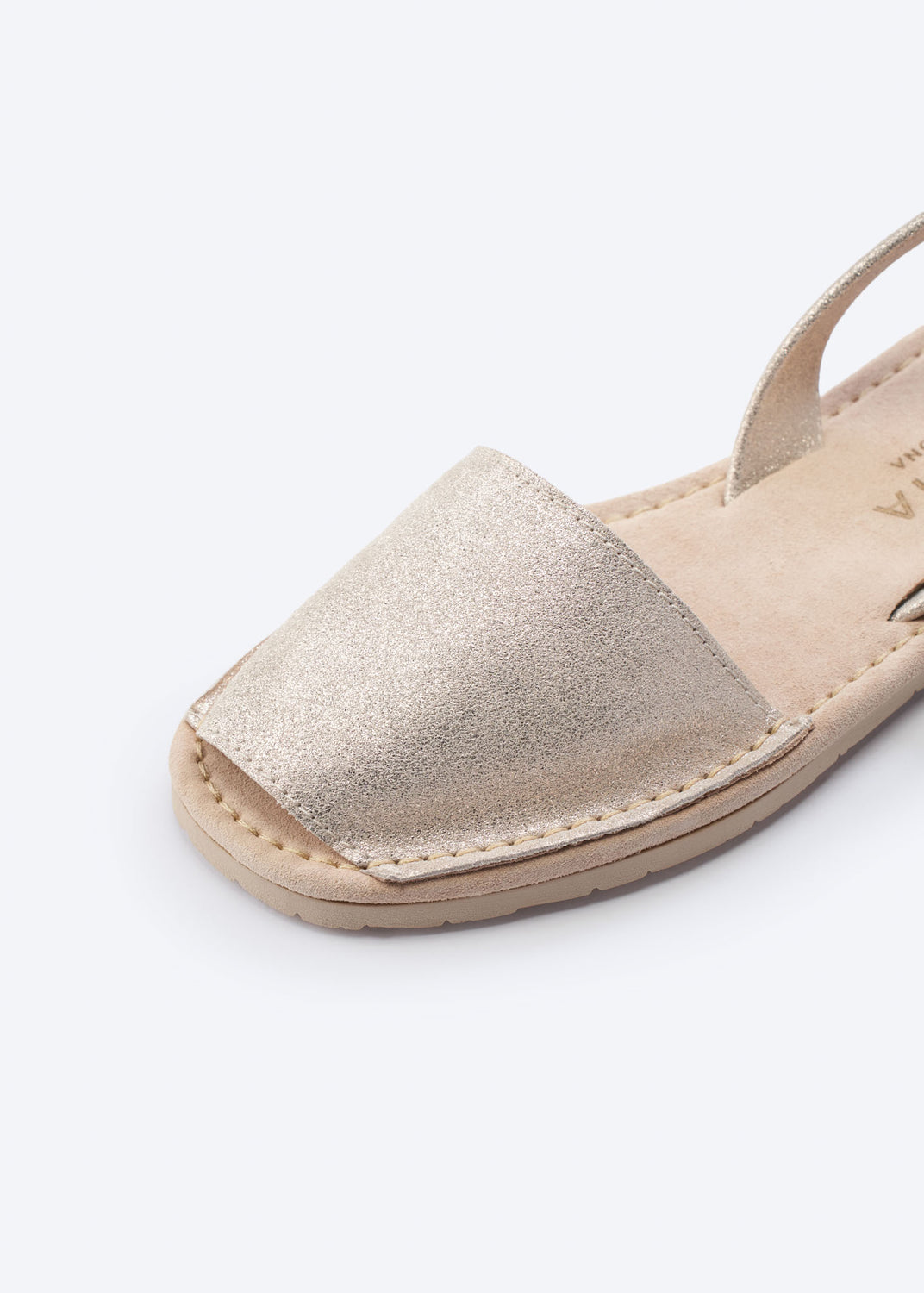 Close-up of a metallic gold leather espadrille sandal featuring hand-stitched edging, open-toe front, and a cushioned flat sole.