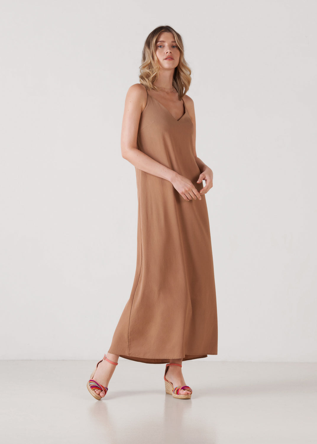 Full-length model wearing pink suede ankle-strap wedge espadrille sandals with multicolor straps and a jute platform