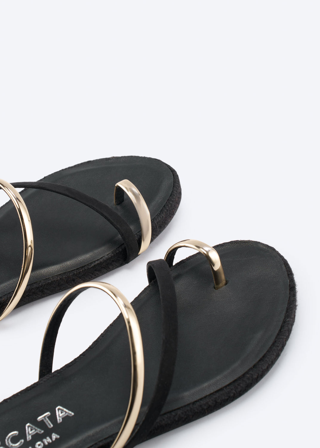 Detail of black flat sandals with gold-tone strap accents.
