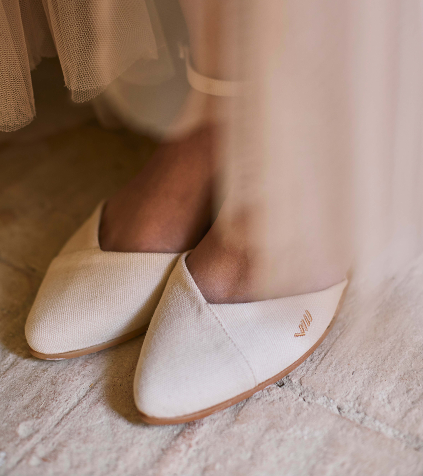 Ivory beige espadrille flats styled beneath a flowing tulle dress in a softly lit Mediterranean interior.