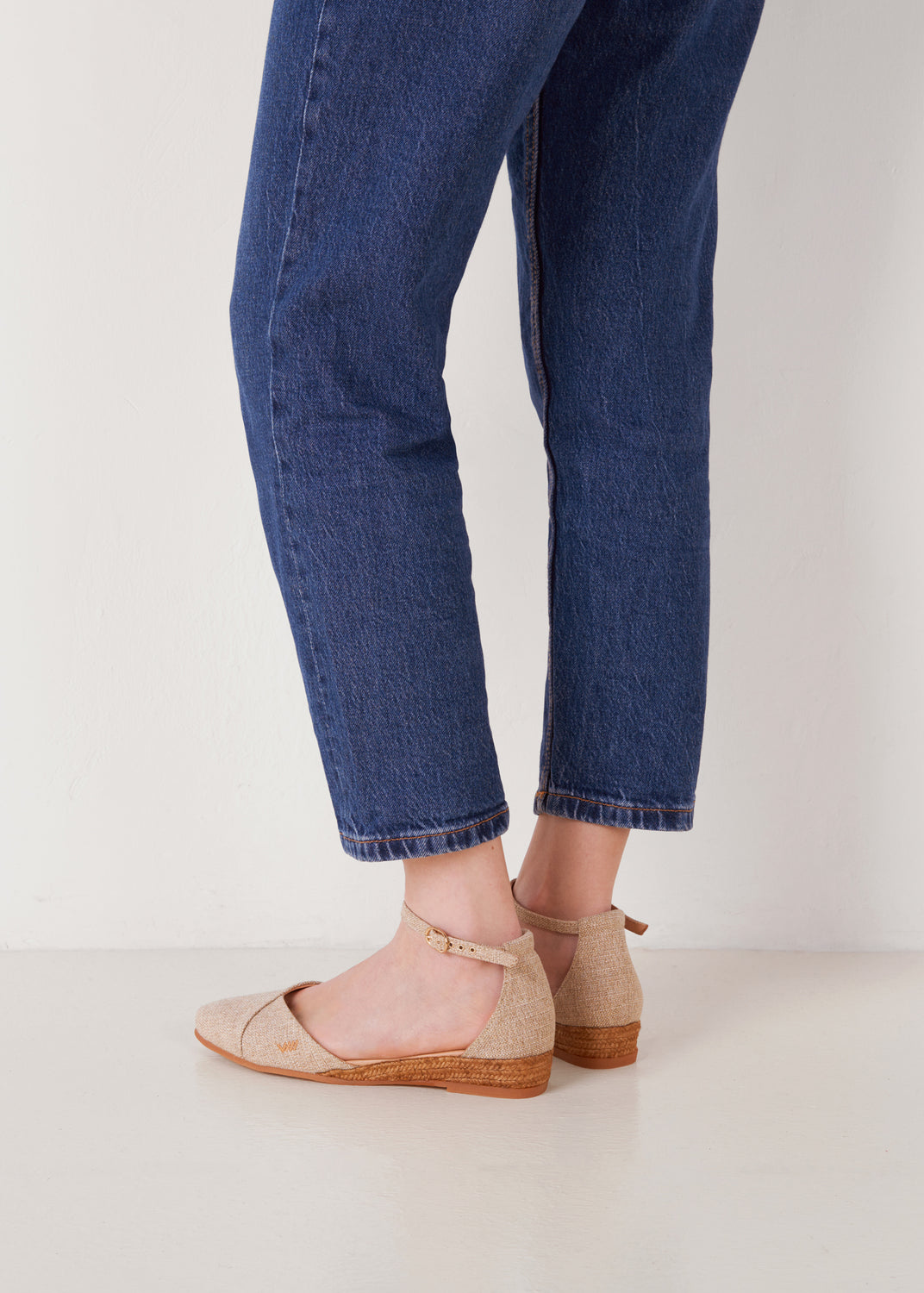 Side view of silver canvas ankle-strap flat espadrilles with a natural jute sole, worn with blue jeans