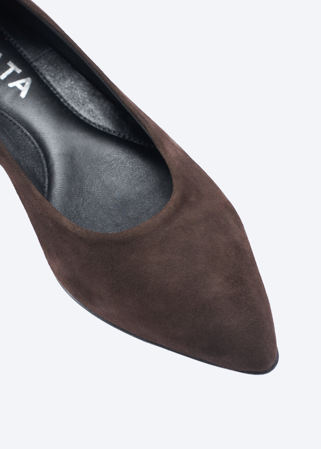 A close-up of a dark brown suede pointed-toe pump shoe, showing the textured upper and black interior insole with partial white branding text.