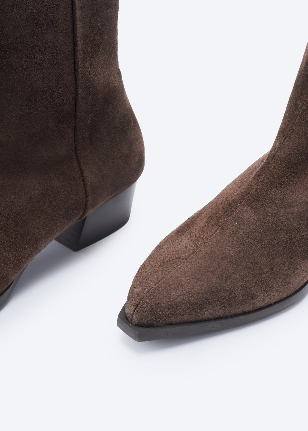 Close-up of a pair of dark brown suede pointed-toe ankle boots with low block heels, shown on a clean white background.
