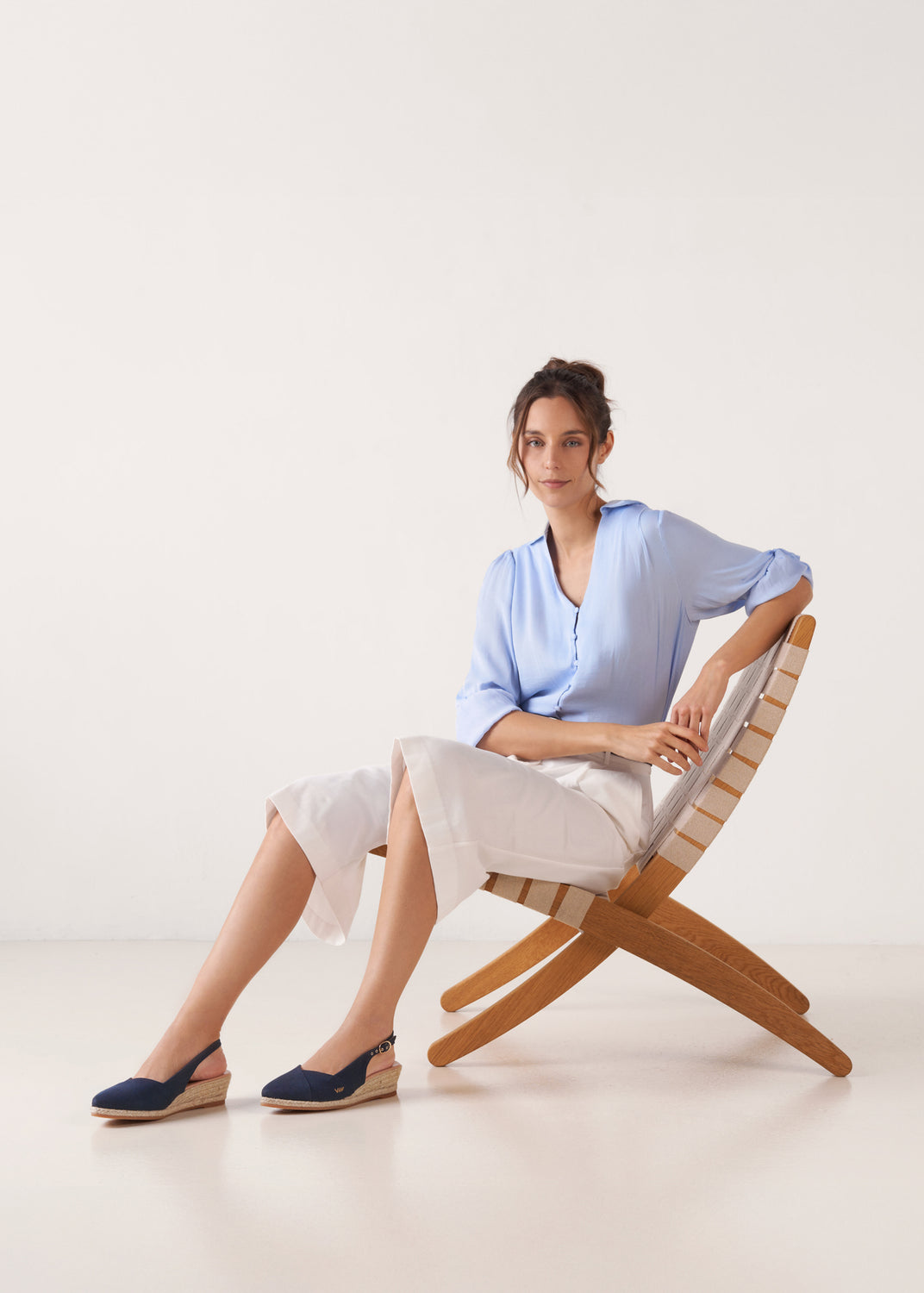 Model seated wearing navy blue canvas slingback low wedge espadrilles with a natural jute platform