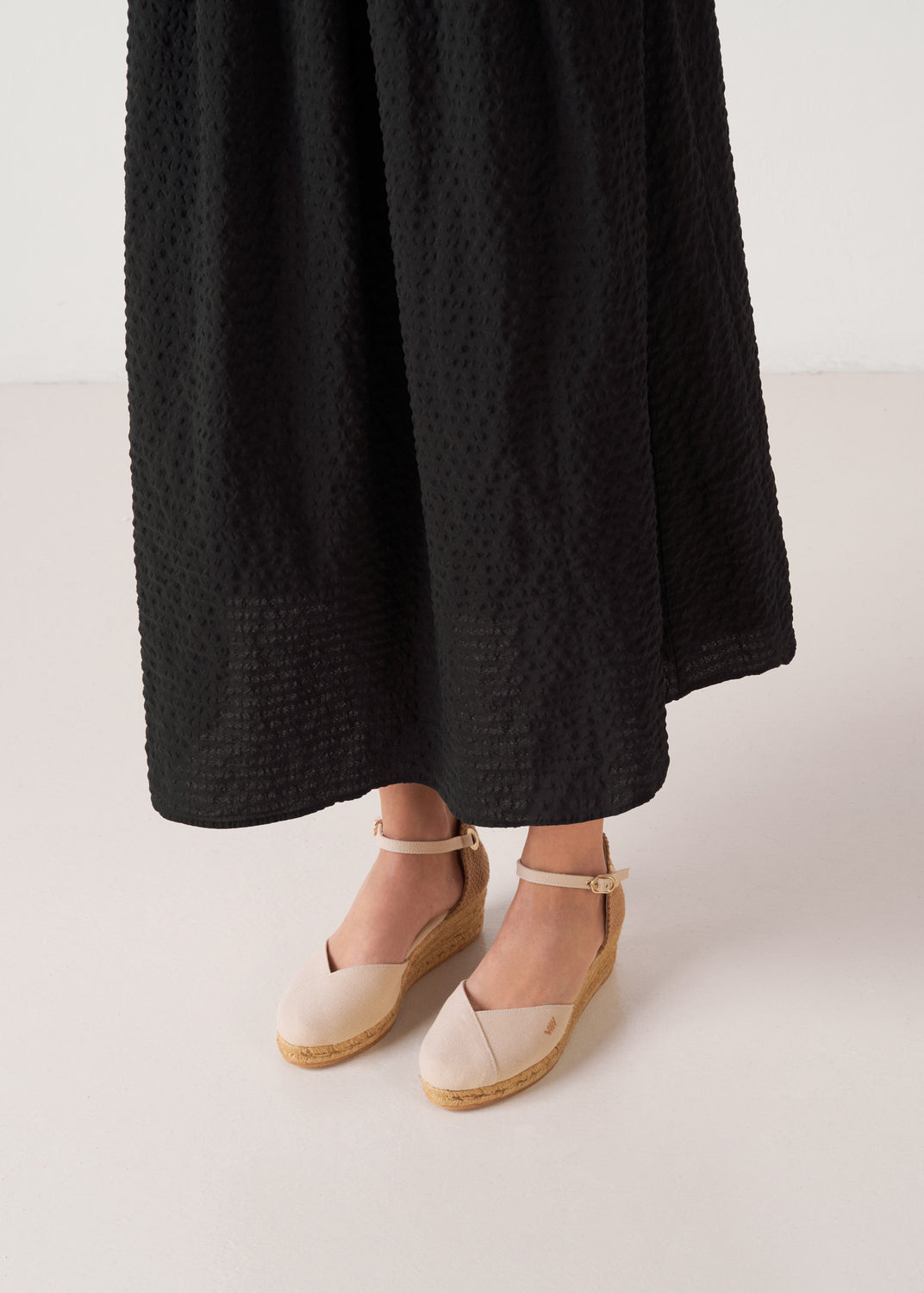 Beige canvas ankle-strap wedge espadrilles with a natural jute platform, styled with a black midi dress