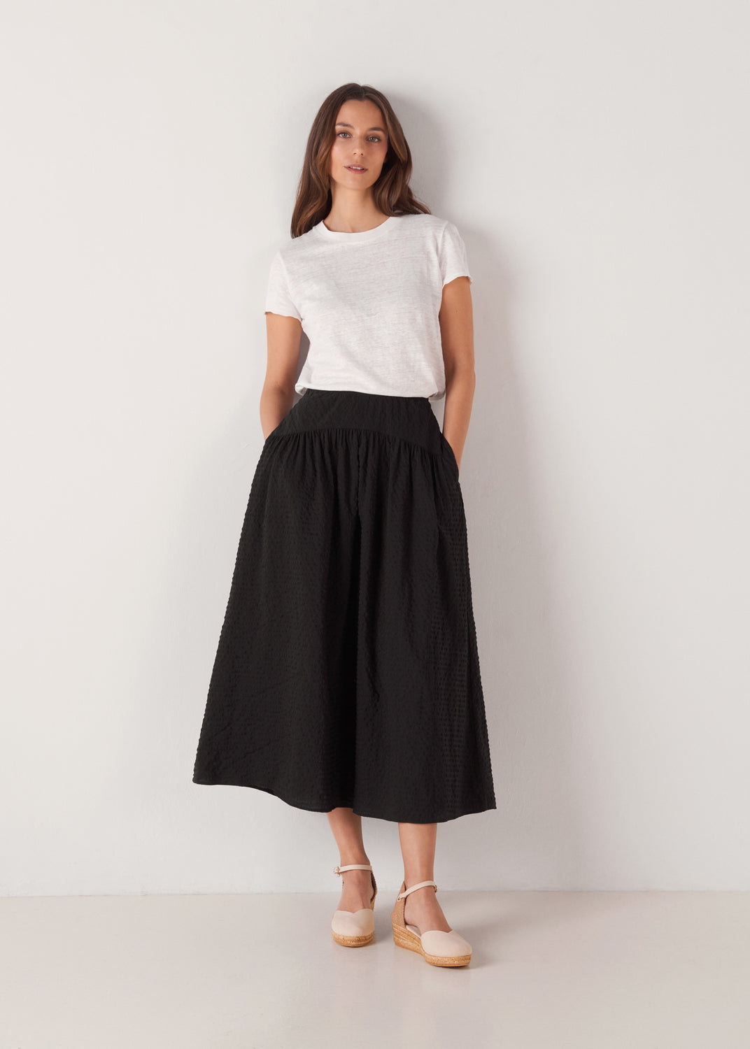 Full-length model wearing beige canvas ankle-strap wedge espadrilles with a natural jute platform