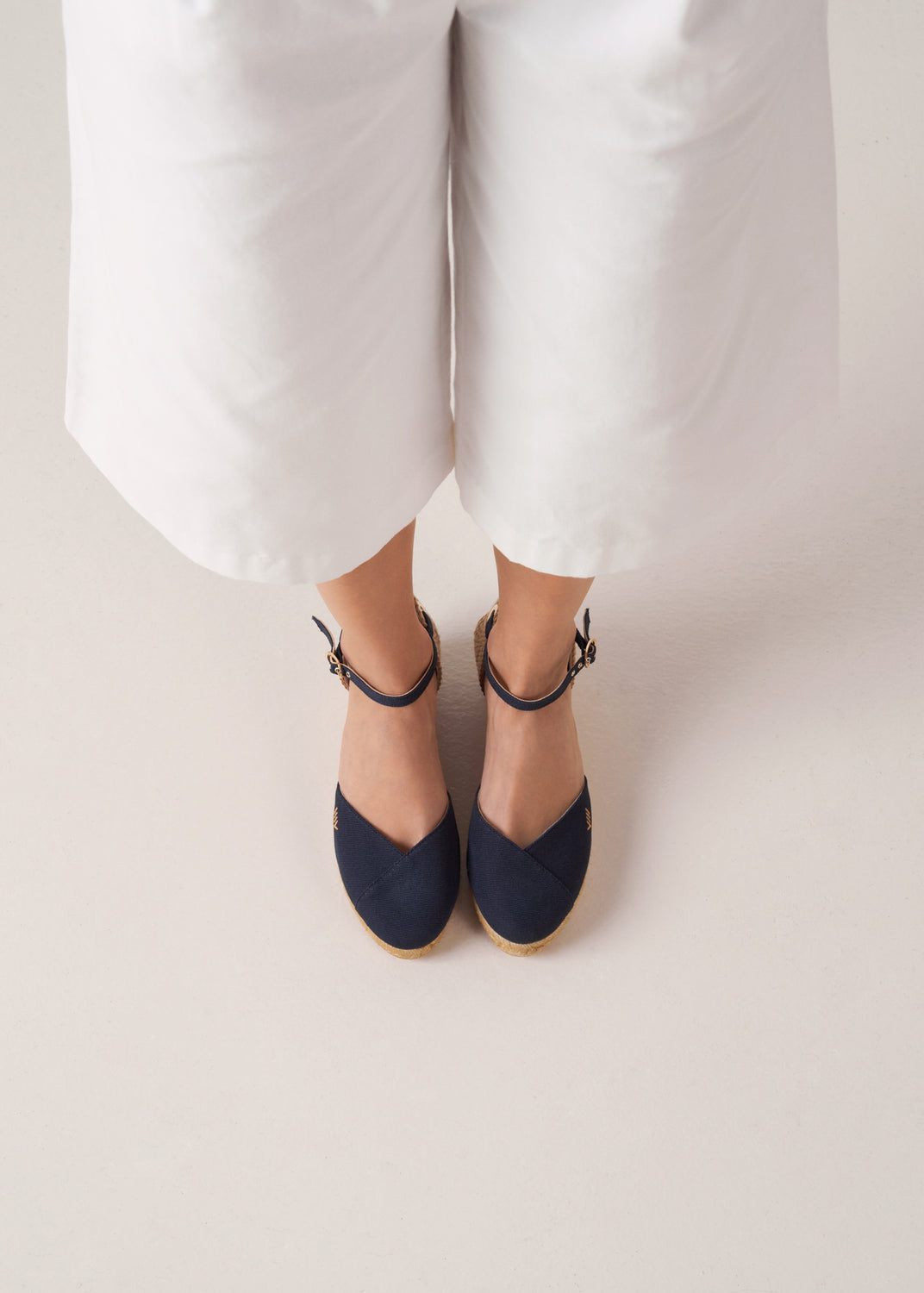 Top view of navy canvas ankle-strap wedge espadrilles with a natural jute platform on model