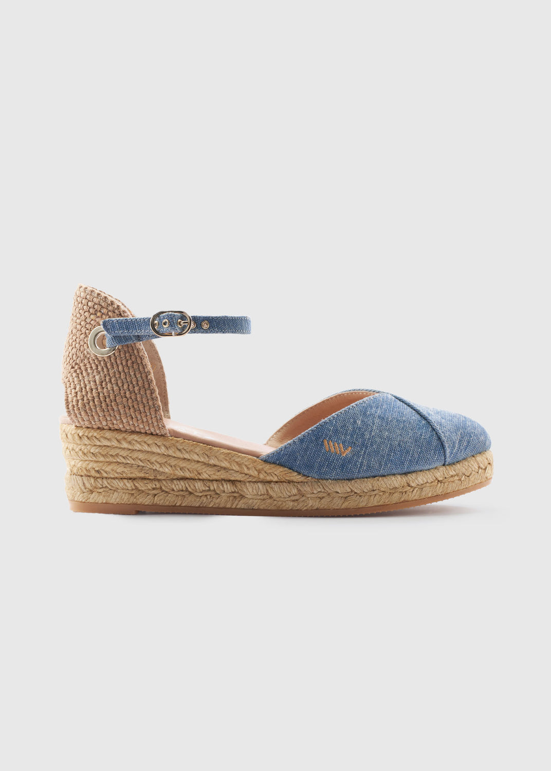 Side view of washed denim low wedge espadrille with an ankle strap, closed toe, and natural braided jute wedge, handcrafted in Spain