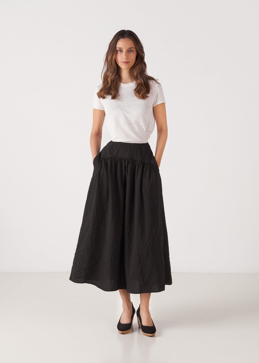 Full-length model wearing black suede slip-on wedge shoes with a natural cork sole