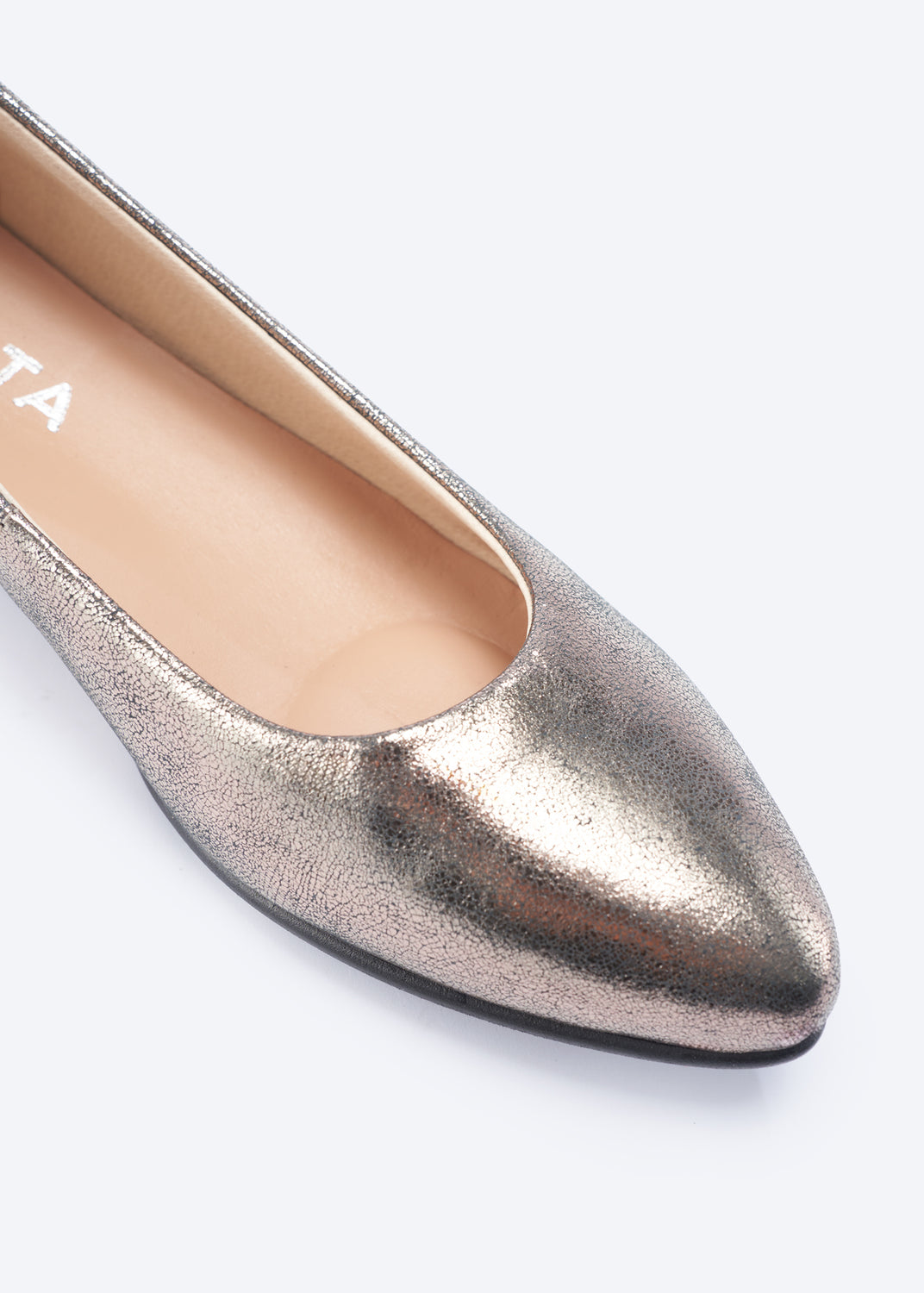 A close-up of a metallic rose gold pointed-toe flat shoe, showing the textured metallic upper, beige insole, and a sliver of black outsole against a light gray background.
